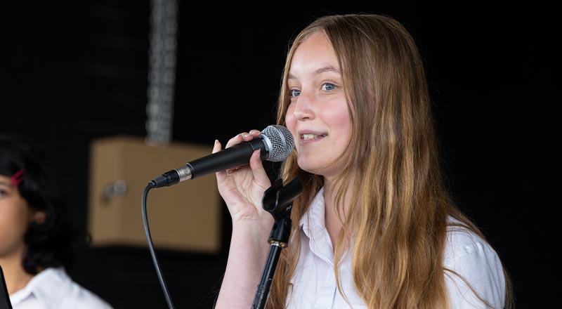 St Clare's Hassall Grove student singing. She is on stage and holding a microphone